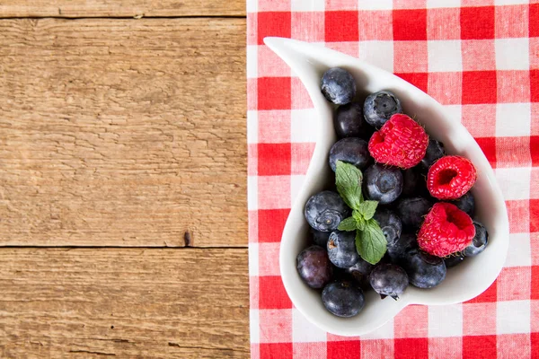 Blueberries and raspberries in the white dish on wood — Stock Photo, Image