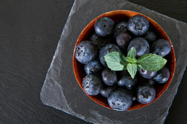 Blueberries with fresh mint leaves on black slate board. — Stock Photo, Image