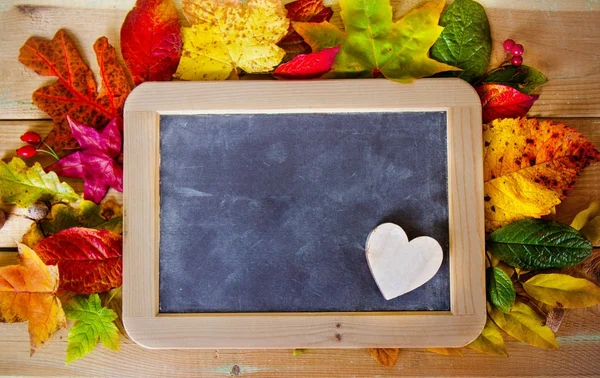 Blackboard with autumn leaves on the table — Stock Photo, Image