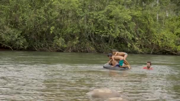 Niños indígenas y un adulto juegan en un río con un neumático flotante — Vídeos de Stock