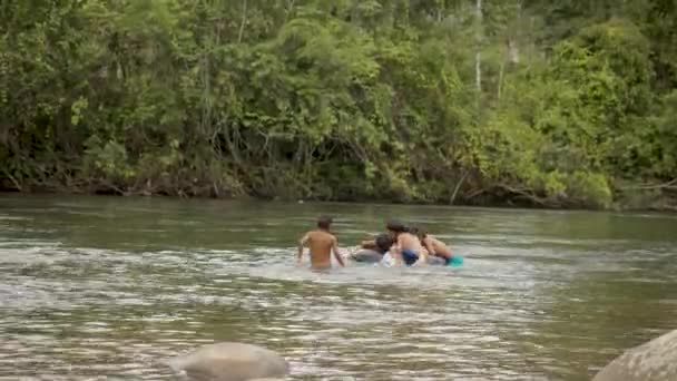 Les garçons autochtones jouent dans une rivière avec un pneu flottant — Video