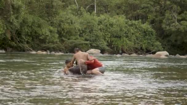 Niños indígenas y un hombre extranjero juegan en un agua con un neumático flotante — Vídeos de Stock