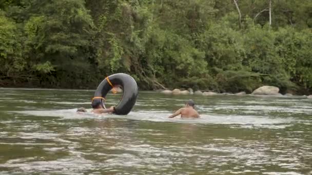 Meninos indígenas e um homem estrangeiro estão segurando um pneu flutuante — Vídeo de Stock