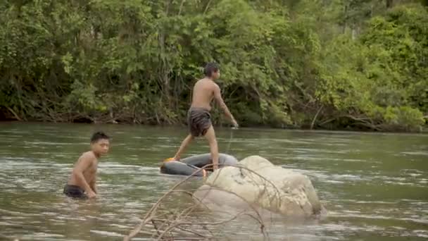 Deux garçons autochtones jouent dans l'eau avec un pneu flottant — Video