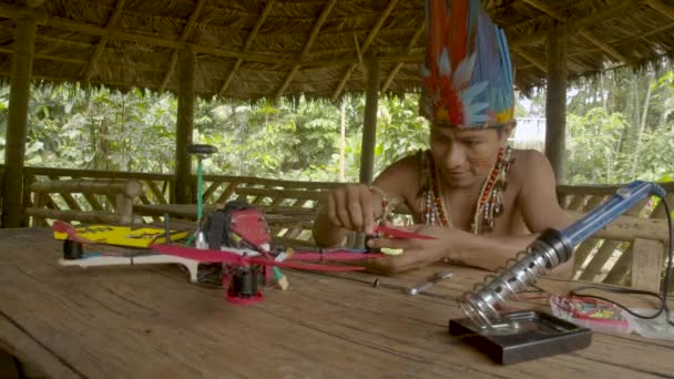 O homem indígena está construindo um drone enquanto está sentado em sua cabana — Vídeo de Stock