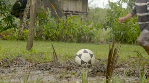 Küçük yerli çocuk çamurlu bir futbol sahasında topa vuruyor. — Stok video