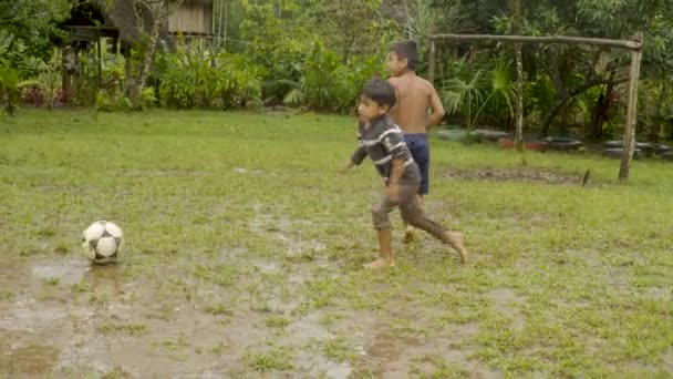 Zwei junge indigene Jungen spielen Fußball auf einem matschigen Platz — Stockvideo