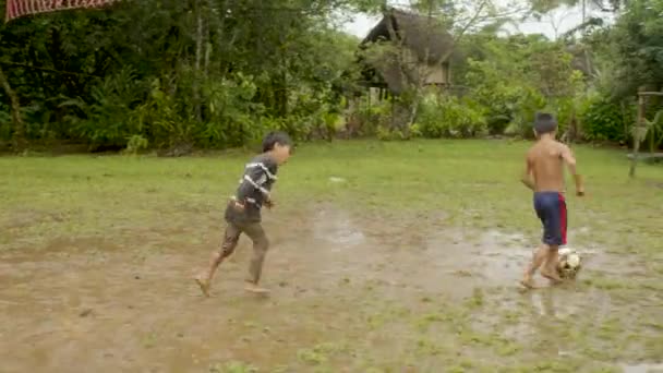 Deux jeunes garçons autochtones jouent au football sur un terrain de leur village — Video