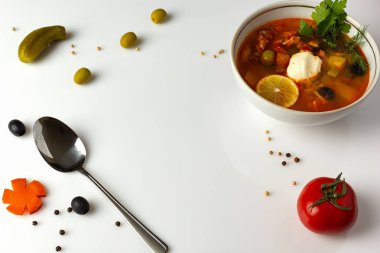 Beyaz arka planda, bir tabak çorba, salatalık, domates, biber, kaşık, baharatlar..