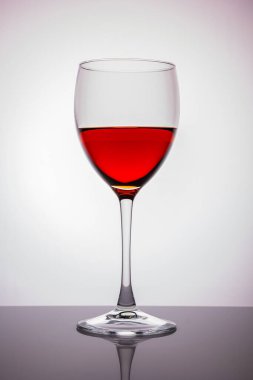 Ayakta duran bir bardak. Cam bir masada ve beyaz bir arka planda duran ücretsiz bir bardak kırmızı şarap..