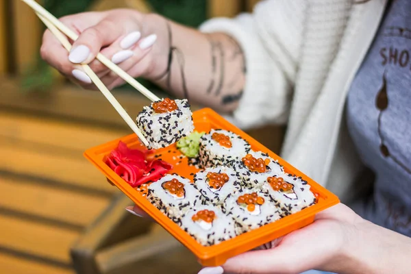 Woman hand is holding bamboo sticks and takes one sushi by it on legs, top view