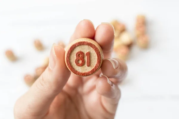 Human hand with a Lotto barrel number 81. Play bingo or Lotto on a wooden table. Concept of Board games. Ideas for leisure at home in isolation with the family.