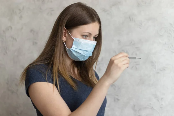 Upset, displeased girl in medical face mask with thermometer. Flu, cold, virus, fever and coronavirus symptoms. Woman measured her body temperature. Attractive girl feels unwell and getting sick.