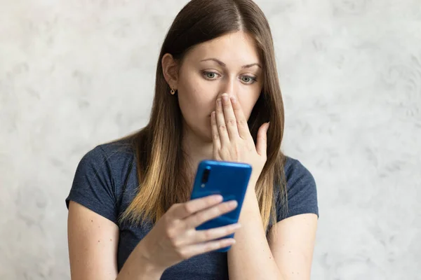 Woman watching shocking video online on her mobile phone. Young girl looking at phone seeing bad news or photos. Girl pleasantly surprised and excited.