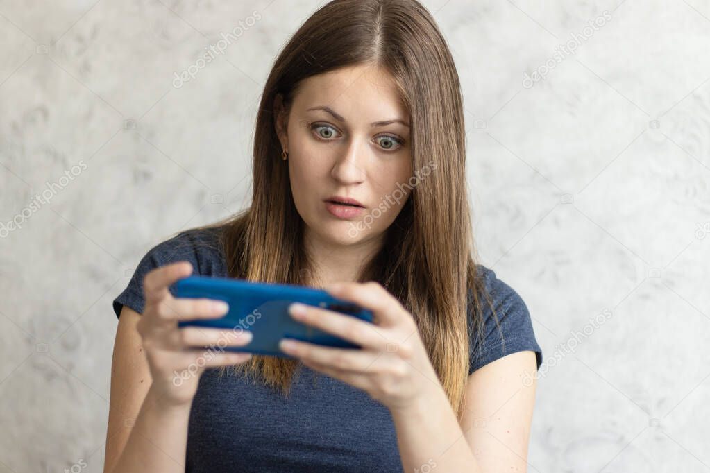 Woman watching shocking video online on her mobile phone. Young girl looking at phone seeing bad news or photos. Girl pleasantly surprised and excited