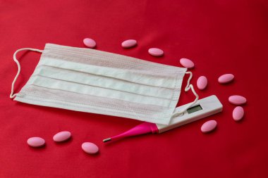 kırmızı zemin üzerinde tıbbi maske, tabletler ve termometre