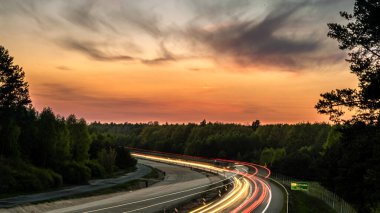 Ormanın arka planında gün batımında araba ışıkları