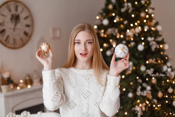 Schöne sexy junge Frau in weißem Pullover sitzt neben weißem Weihnachtsbaum und hält Geschenk. Weihnachtsfoto — Stockfoto