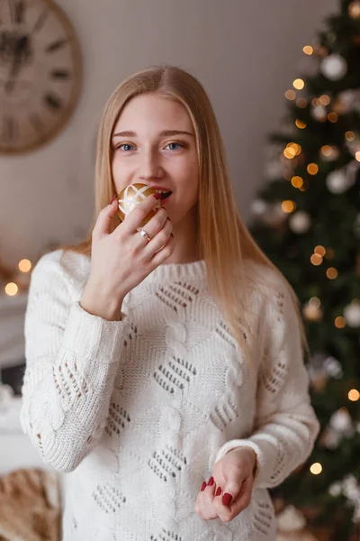 Hermosa mujer joven sexy en suéter blanco sentado al lado del árbol de Navidad blanco, sosteniendo presente. Foto de Navidad —  Fotos de Stock