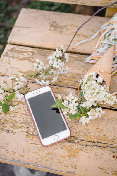 phone on a yellow wooden background with a sprig of a blossoming apple tree