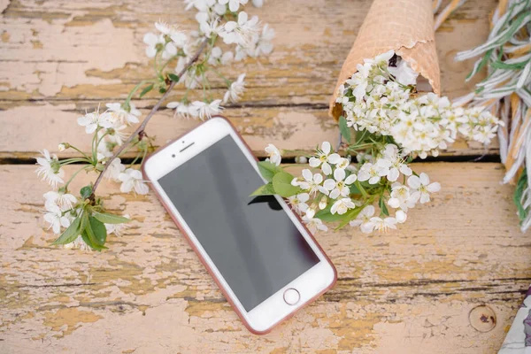 Telefono su uno sfondo di legno giallo con un rametto di un melo fiorente Foto Stock