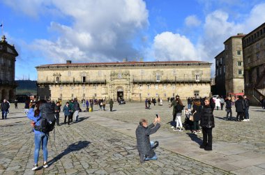 Seyyahlar, Camino de Santiago 'nun son aşamasında fotoğraf çekiyorlar. Plaza del Obradoiro, Hostal de los Reyes Catolicos ile Katedrale yakın. Santiago de Compostela, İspanya. 1 Aralık 2019.