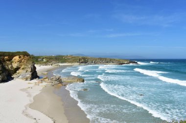 Uçurumlu vahşi sahil, beyaz kum ve dalgalar. Köpüklü turkuaz su, mavi gökyüzü. Viveiro, Lugo, Galiçya, İspanya.