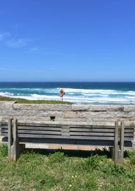 Tahta banklı bir sahil gezintisi. Dalgalar ve mavi gökyüzü ile vahşi deniz. Viveiro, Lugo, Galiçya, İspanya.