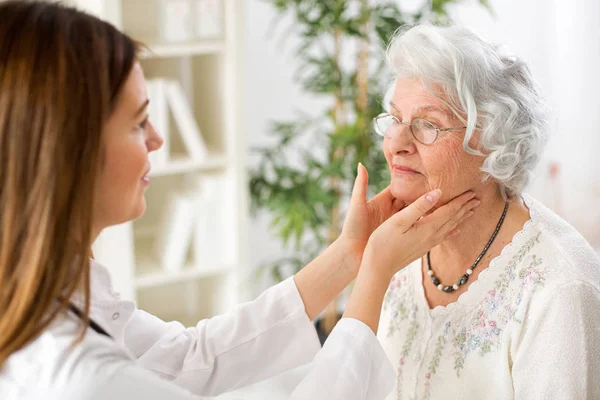 Bella giovane medico esaminando donna anziana ghiandole linfatiche — Foto Stock