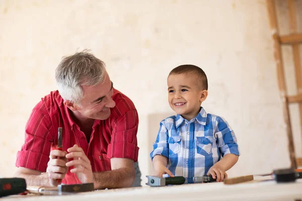 Smiling grandfather and grandson working in workshop — Stock Photo, Image