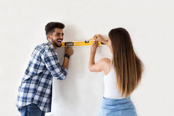 Sonriente pareja joven midiendo pared con herramienta de nivel, renovación —  Fotos de Stock
