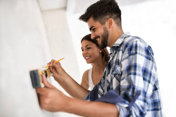 Souriant jeune couple mesurant mur outil de niveau blanc, rénovation — Photo