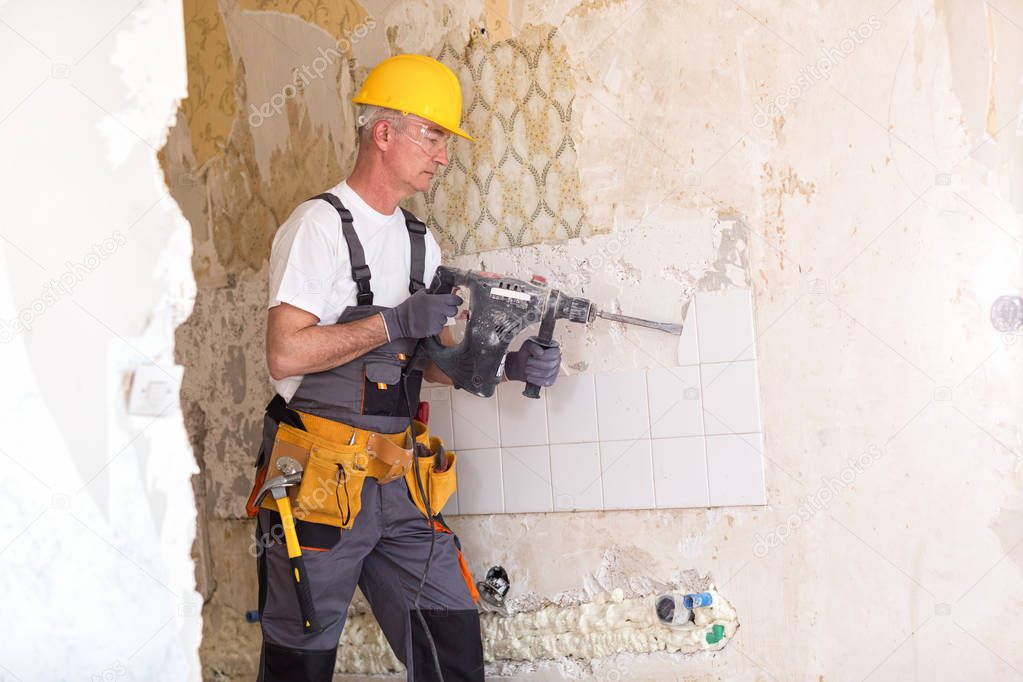 Senior man using drill in the reconstruction of the building