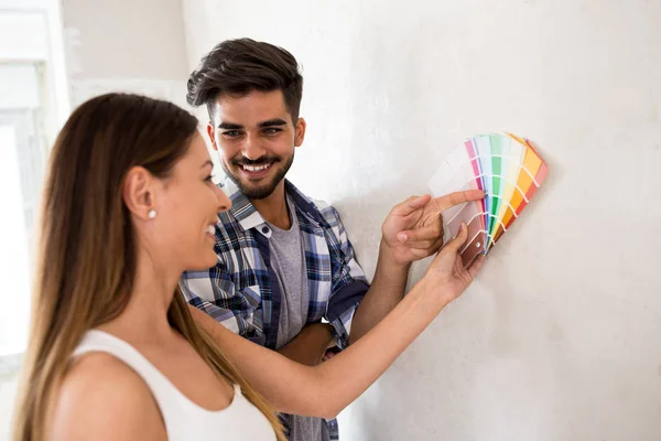 Jeune couple heureux choisissant des couleurs pour peindre leur maison — Photo