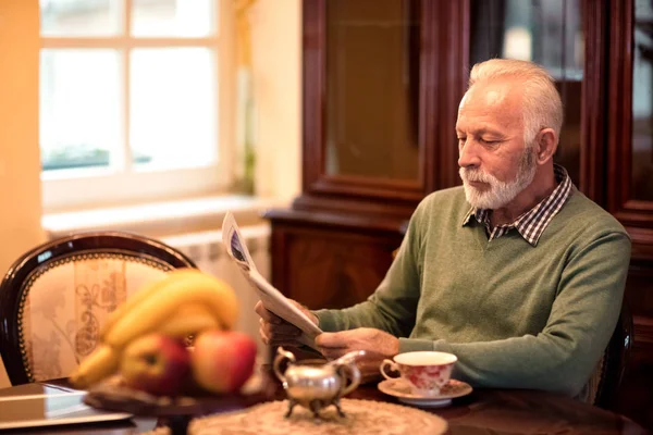 古い年配の男性が自宅で一人で座って、新聞を読む — ストック写真