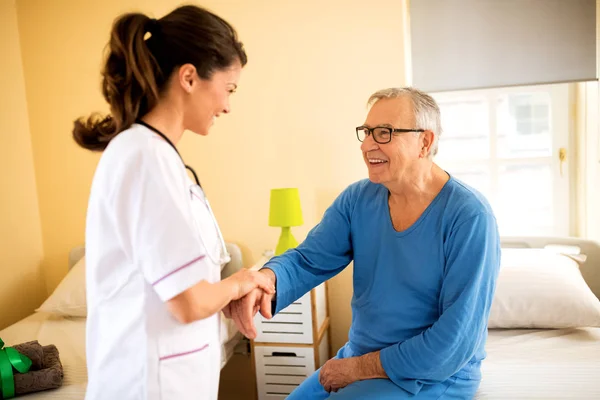 Careful young nurse helps senior patient to stand up — Stock Photo, Image