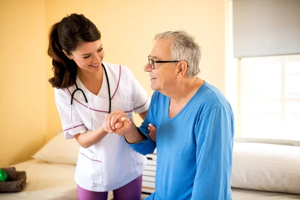 Careful young nurse helps senior patient to stand up — Stock Photo, Image