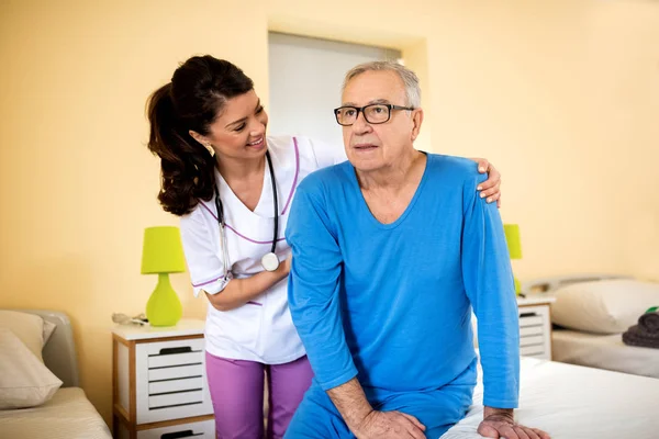 Very patient nurse helps old senior man to stand up from bed — Stock Photo, Image