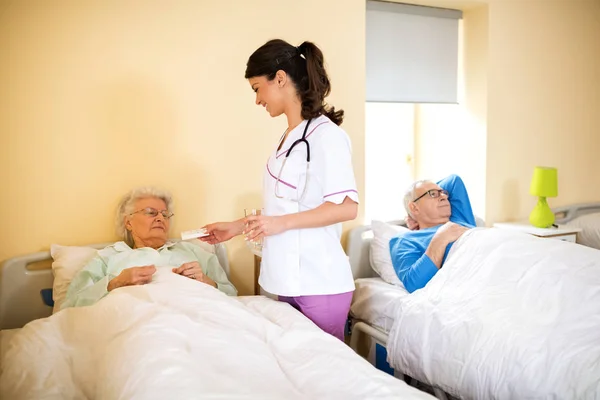 Nurse at nursing home brings medicine to senior immobile woman — Stock Photo, Image