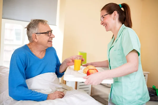 Happy Old Senior Man Looking Careful Nurse While She Brings — Stock Photo, Image