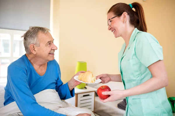 Happy Old Senior Man Looking Careful Nurse While She Brings — Stock Photo, Image