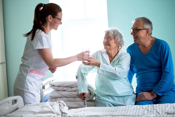 Nursing home, young careful nurse brings water to old woman — Stock Photo, Image