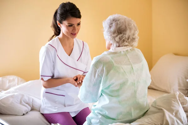 Beautiful nurse holding hand of old senior patient and comfort h