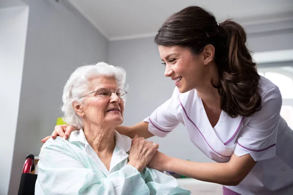 Perawat tersenyum dan wanita tua sabar di kursi roda — Stok Foto