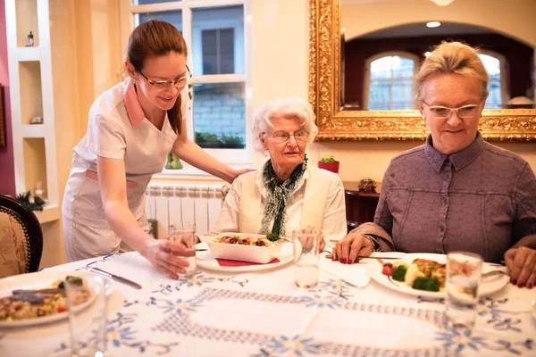 Noggrann sjuksköterska anger en tabell för middag till patienter vid omvårdnad hom — Stockfoto