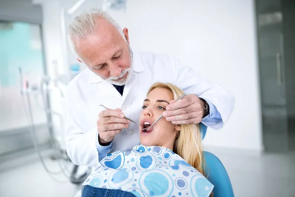 Опытный старший дантист проверяет зубы пациентов — стоковое фото