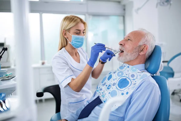 Jovem dentista examinando os dentes de um paciente idoso — Fotografia de Stock