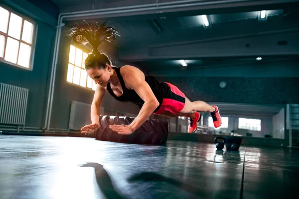 Strong powerful woman doing hard intense crossfit workout at gym, flying push ups