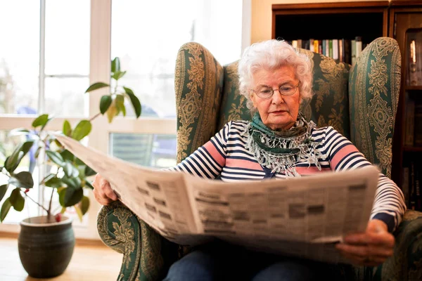 Senior old woman in pansion relaxing at home while reading a newspaper