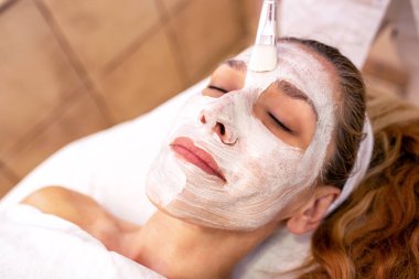 Cosmetician applying a facial layer beauty mask 